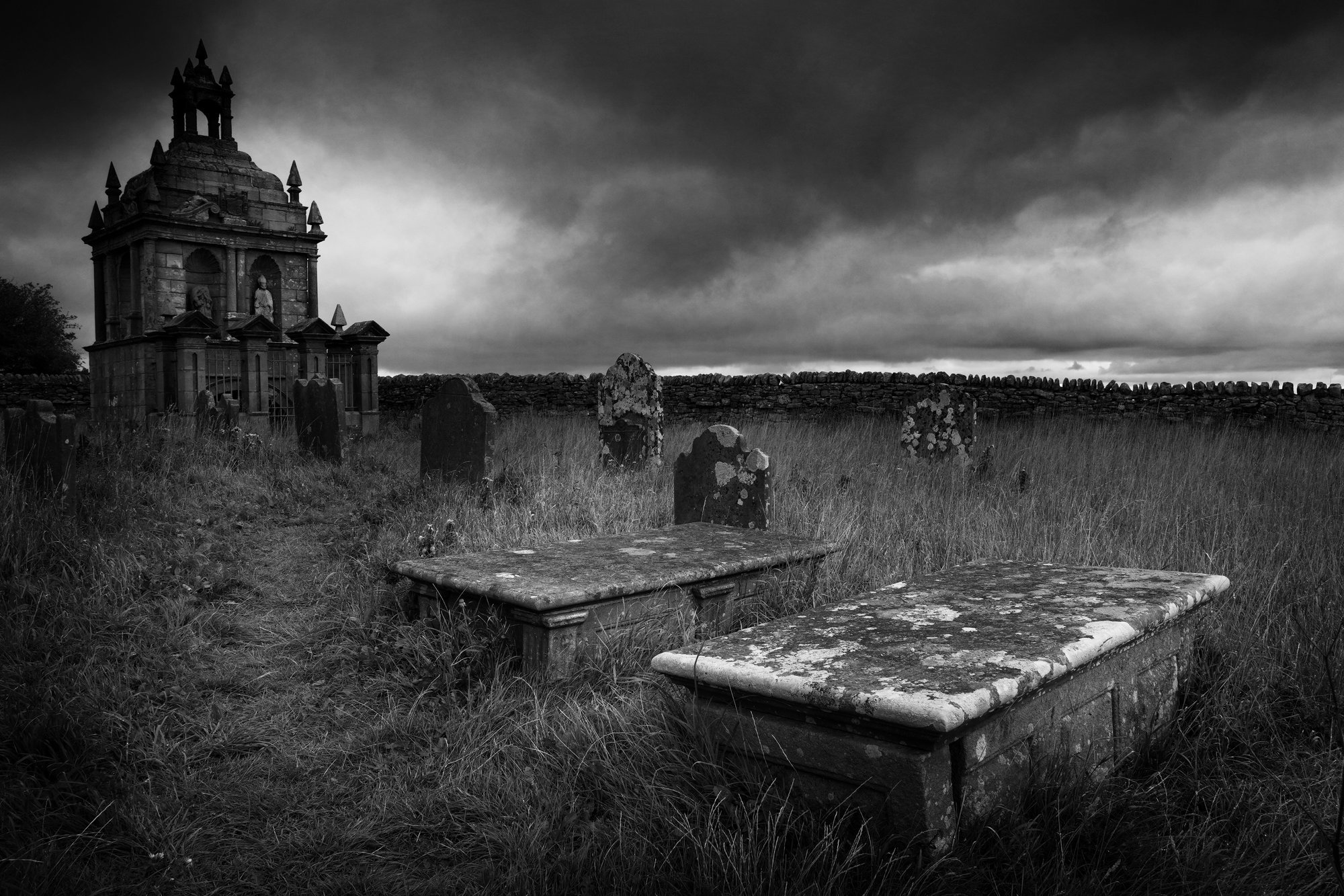 Gothic graveyard with ornate mausoleum under heavy storm clouds