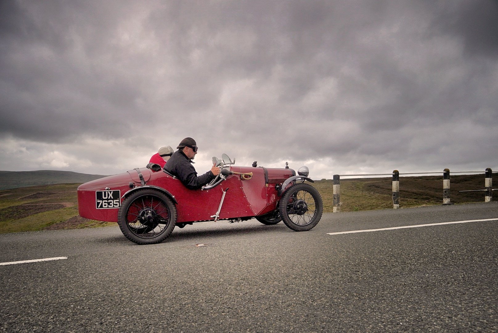 Vintage three-wheeled car on a moorland road under dramatic skies